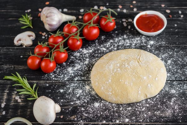 Raw dough for pizza with ingredients and spices on black background